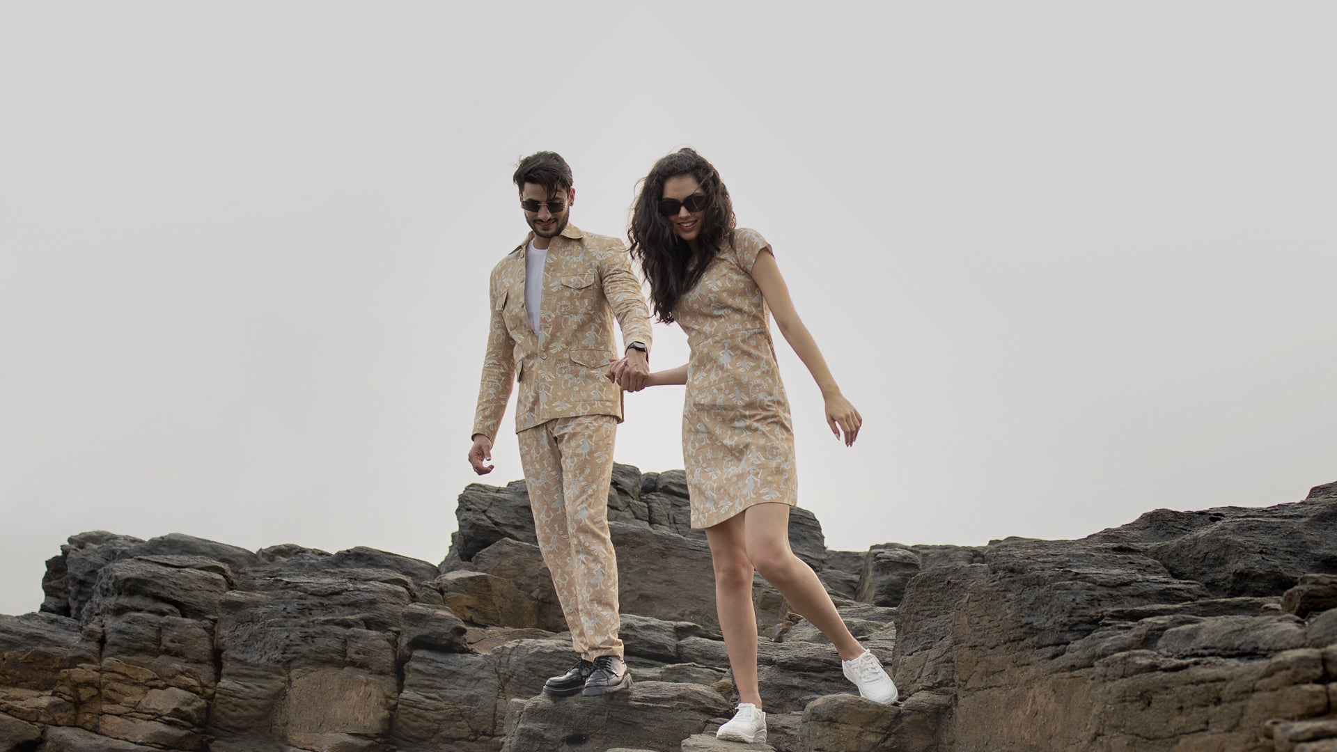 Two people in matching floral outfits standing on rocky terrain.slider_item_BaBtDC
