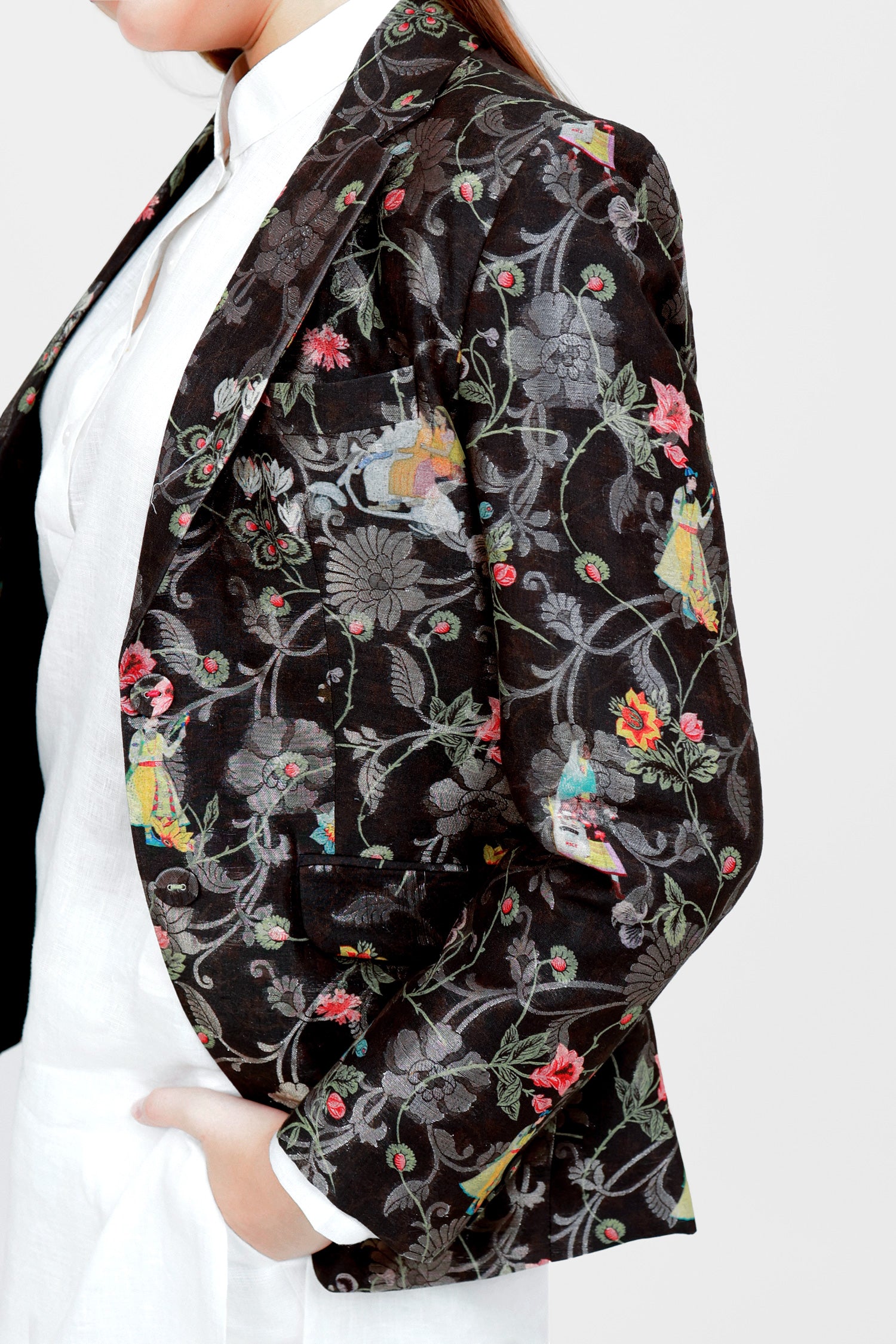 A woman modeling a silk blazer with a floral pattern, wearing a white shirt and pants.