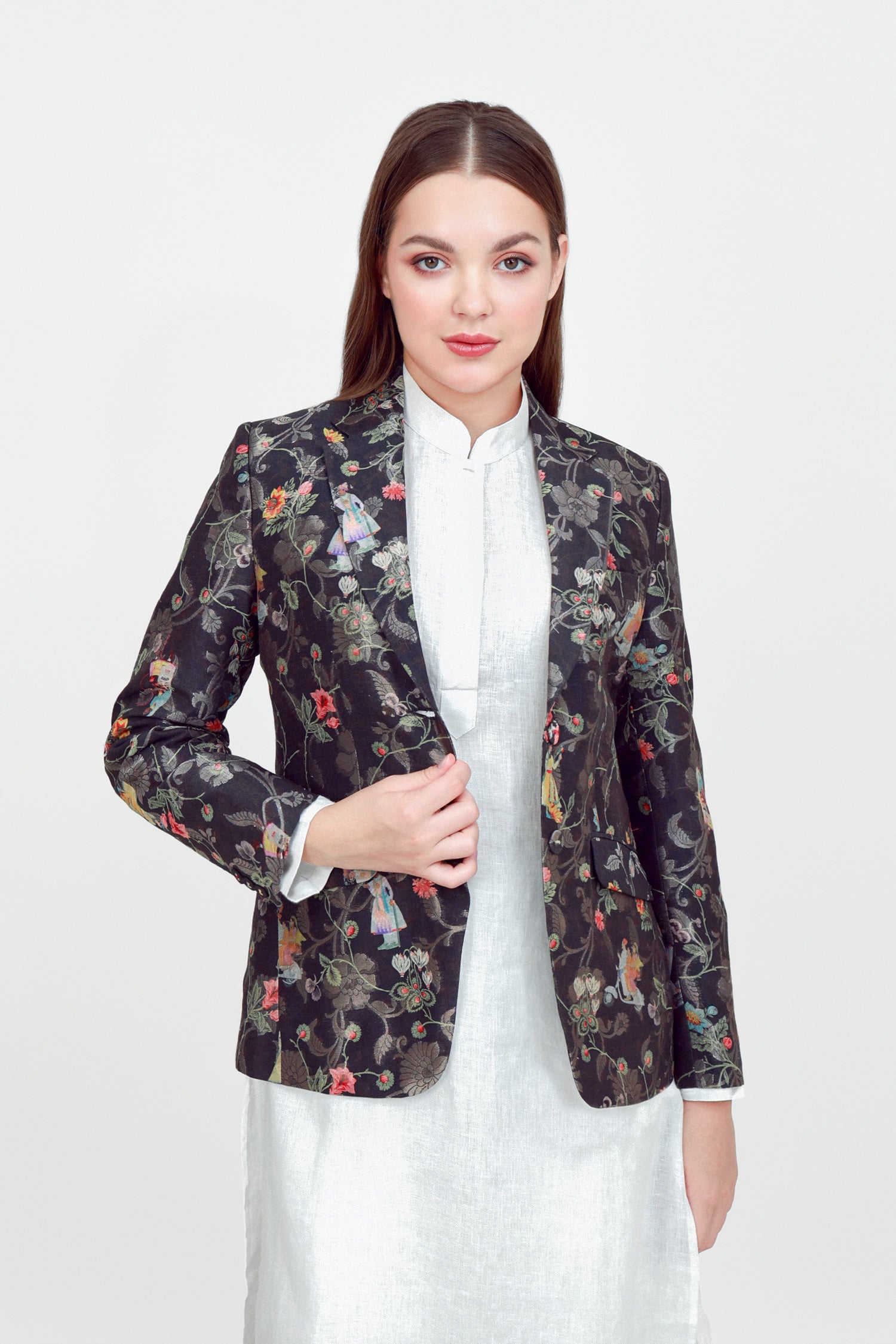 A woman modeling a silk blazer with a floral pattern, wearing a white shirt and pants.