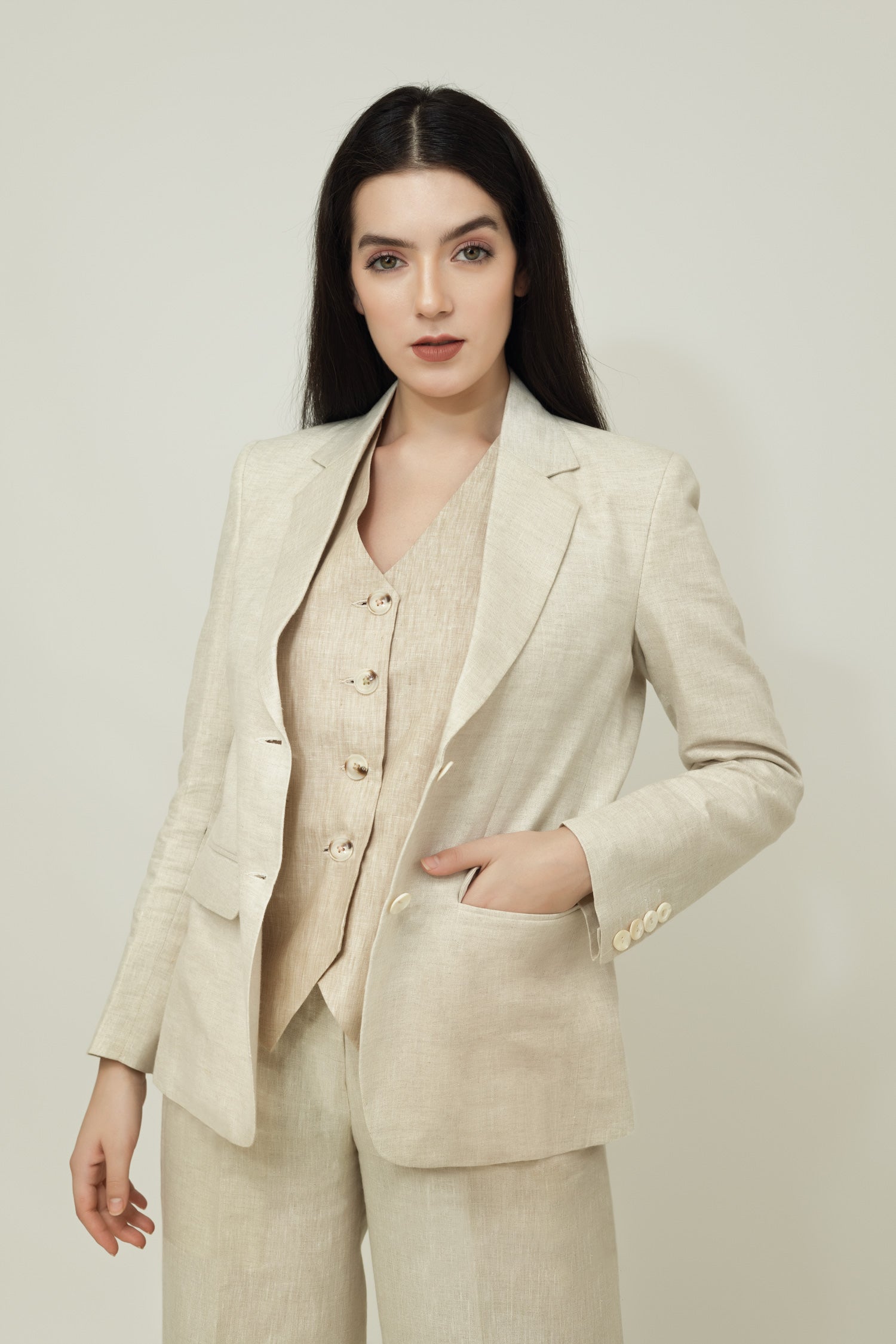 A woman modeling a beige linen blazer with a notch lapel, two-button single-breasted design, and flap pockets.