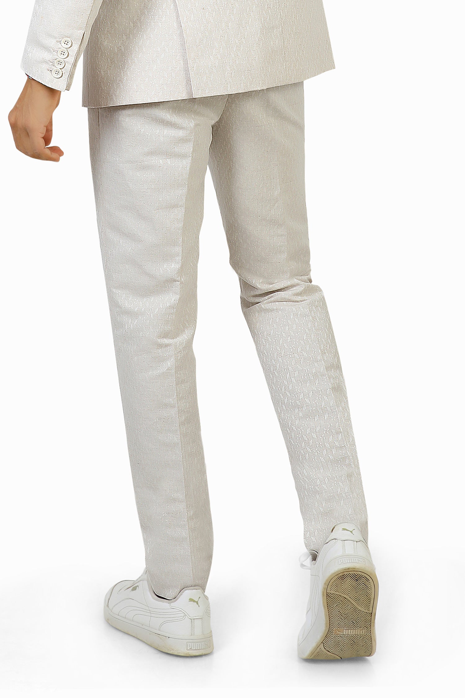 A man wearing white linen trousers with a white jacket and a multicolored shirt, standing against a white background.