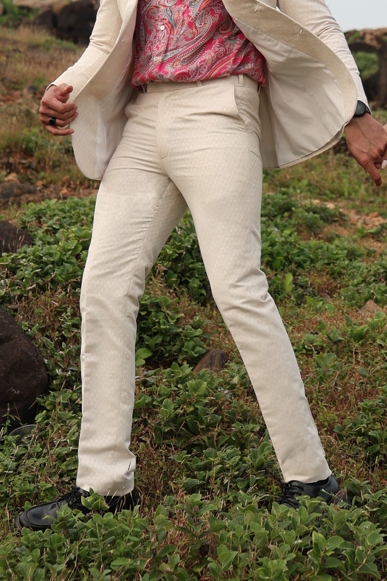 A man wearing white linen trousers with a white jacket and a multicolored shirt, standing against a white background.