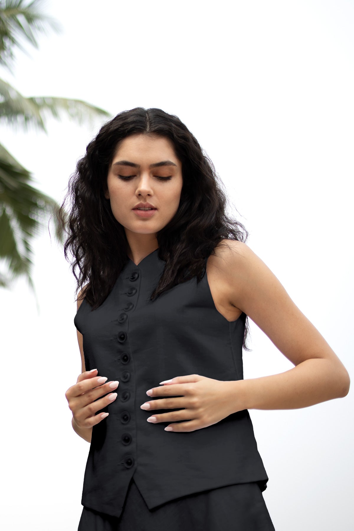 Woman wearing a black sleeveless top with buttons against a white background