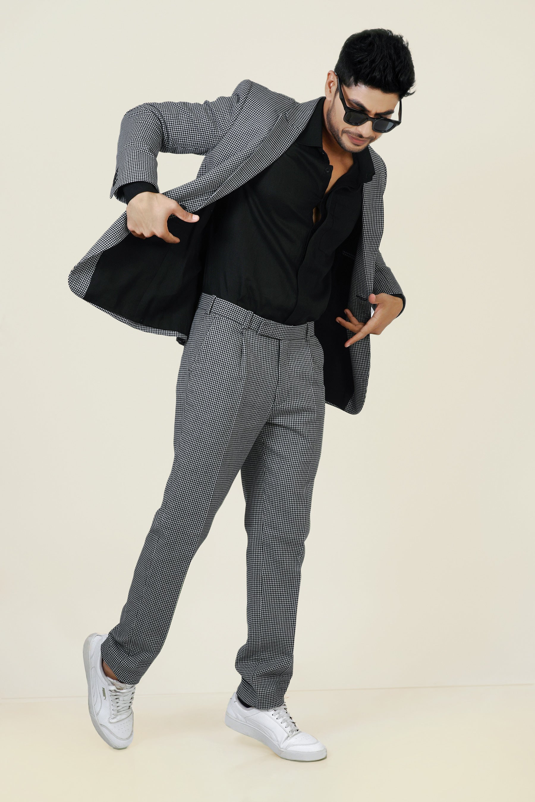 Stylish man in a gray and white checkered cotton jacket and pants, with a black shirt and white sneakers.