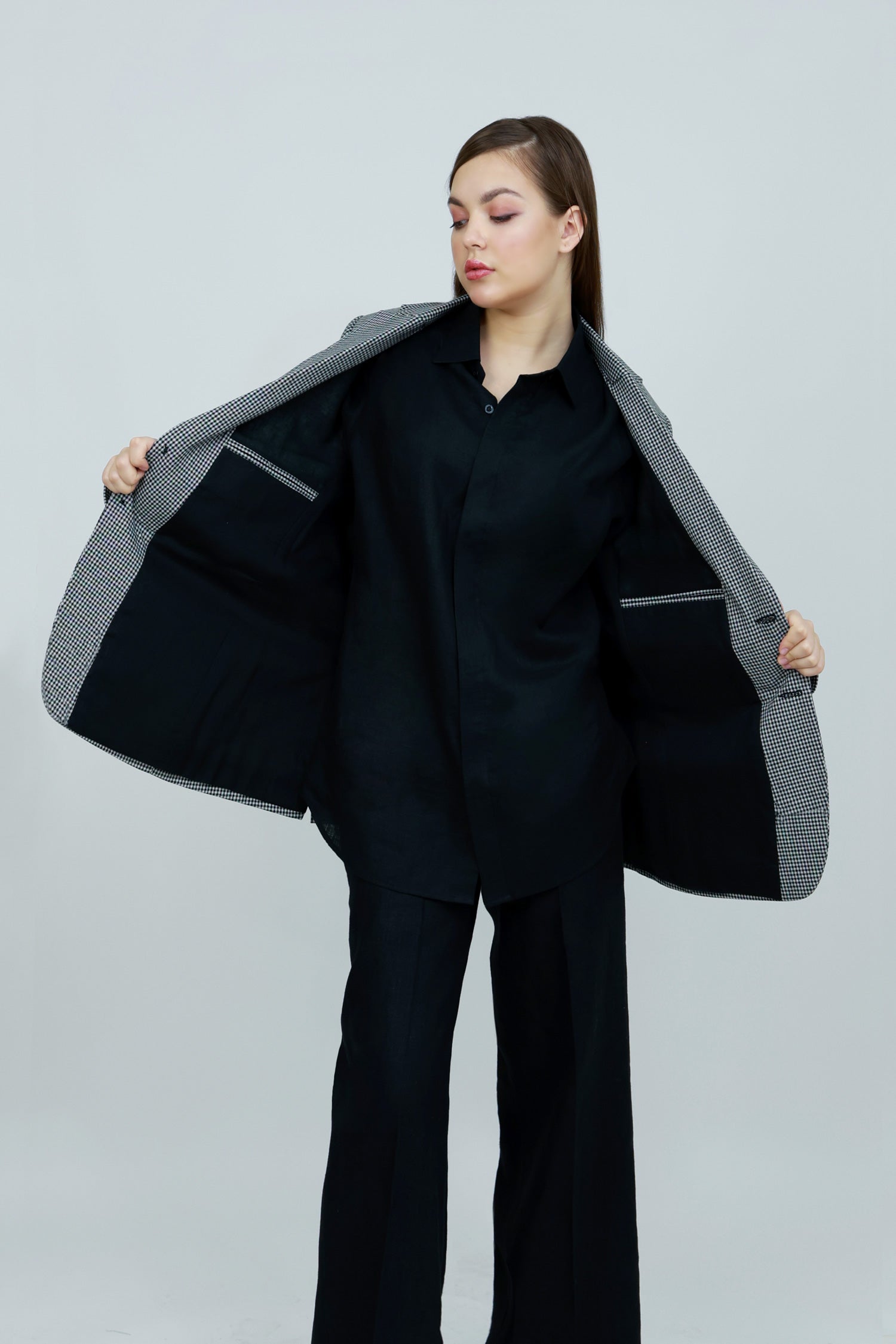 A woman wearing a gray and white patterned cotton blazer, a black button-down shirt, and black wide-leg trousers.