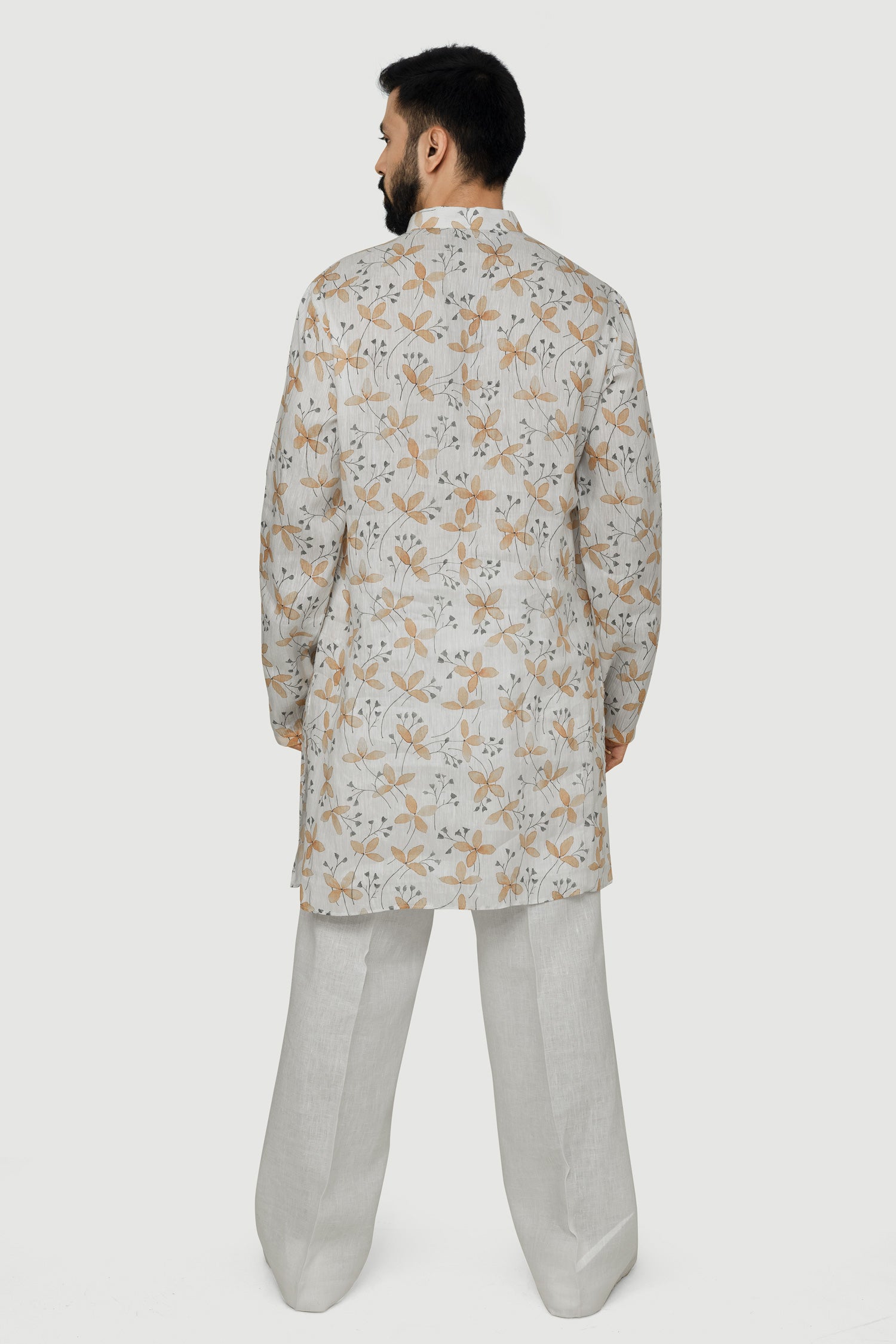 A man wearing a traditional Indian linen kurta with a mandarin collar, featuring a floral print and matching buttons, paired with light-colored trousers.