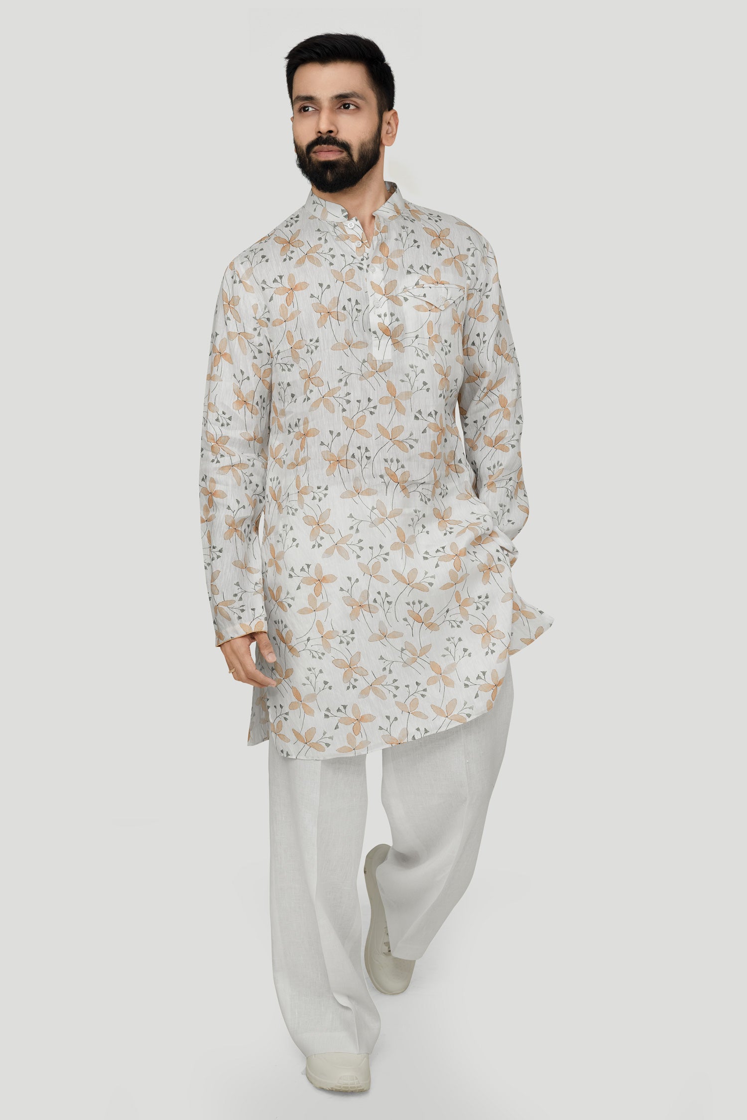 A man wearing a traditional Indian linen kurta with a mandarin collar, featuring a floral print and matching buttons, paired with light-colored trousers.