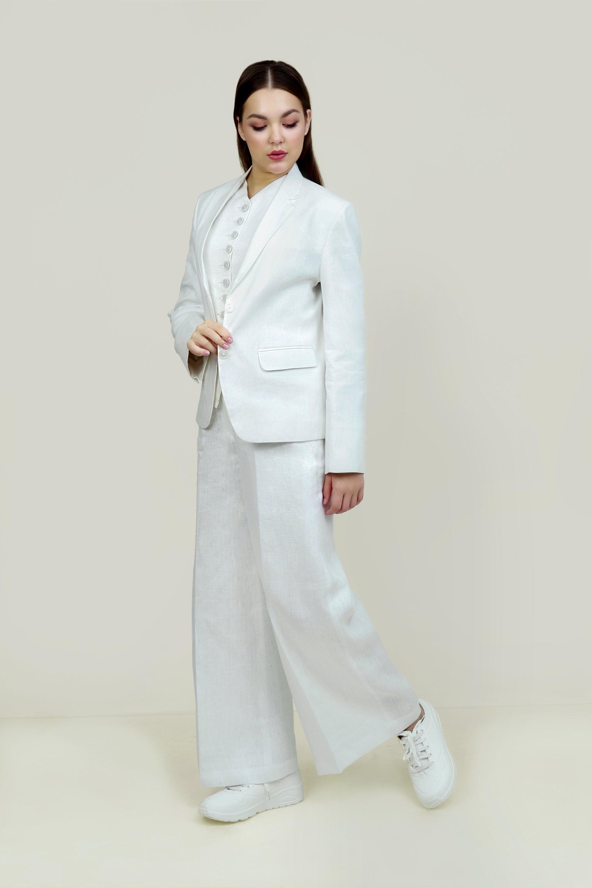 A woman modeling a white linen blazer with a notch lapel, two-button single-breasted design, and flap pockets.