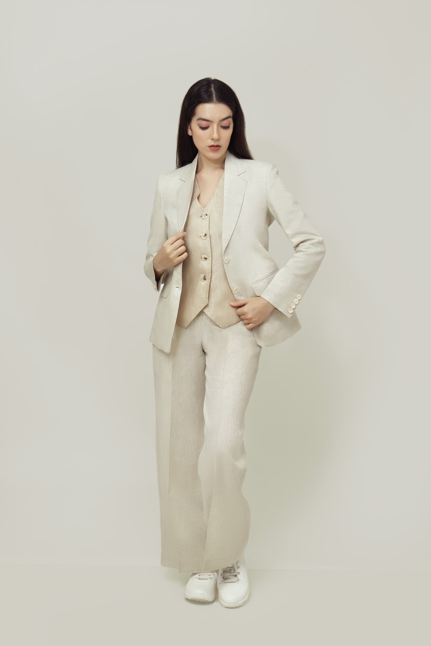 A woman modeling a beige linen blazer with a notch lapel, two-button single-breasted design, and flap pockets.