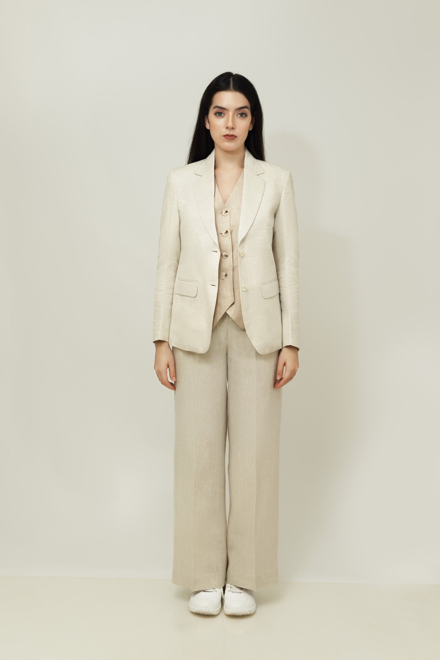 A woman modeling a beige linen blazer with a notch lapel, two-button single-breasted design, and flap pockets.