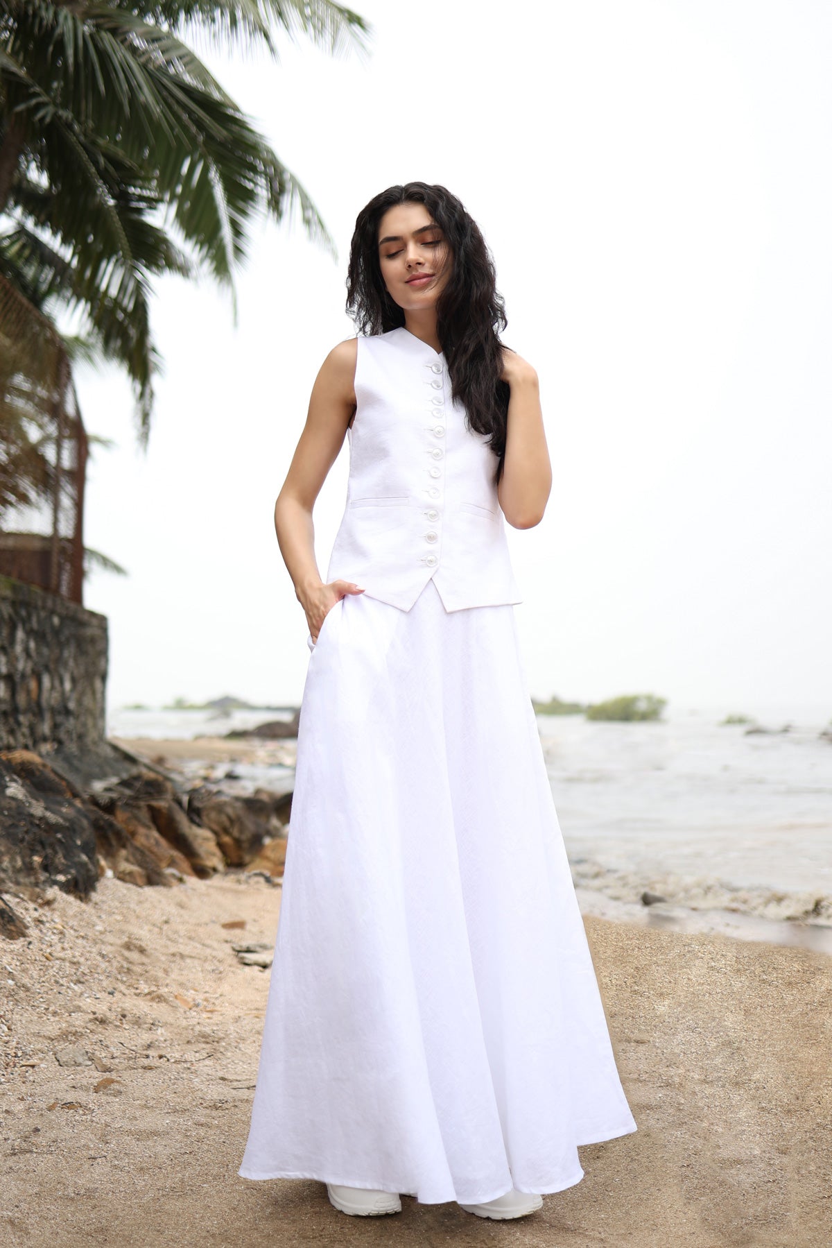 Woman in a white outfit standing on a beach with palm trees in the background