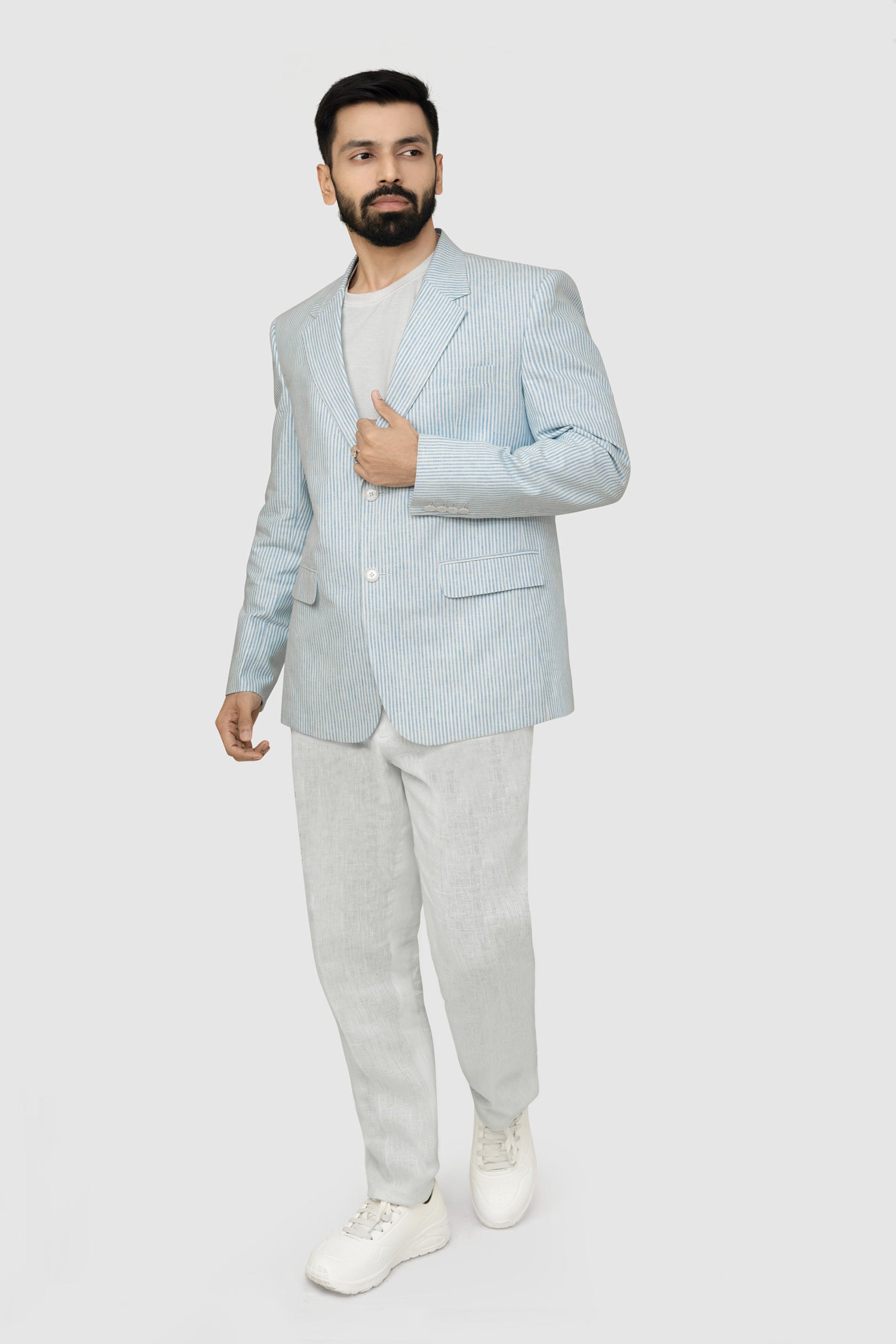 A male model wearing a light blue linen blazer with a Notch Lapel, two buttons, and two patch pockets on the front, paired with light-colored trousers.