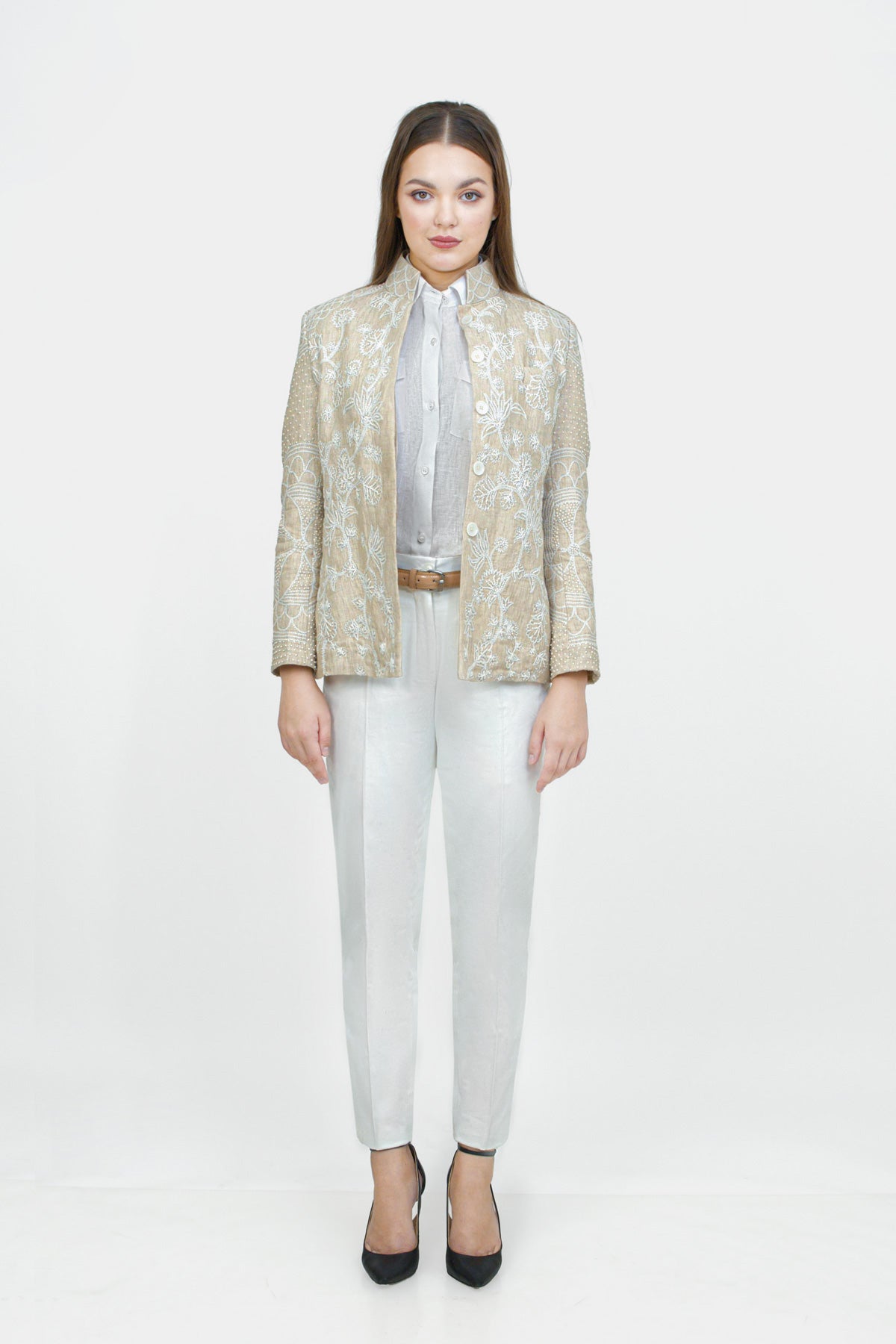 Woman wearing a gold patterned blazer, white shirt, and white pants on a white background