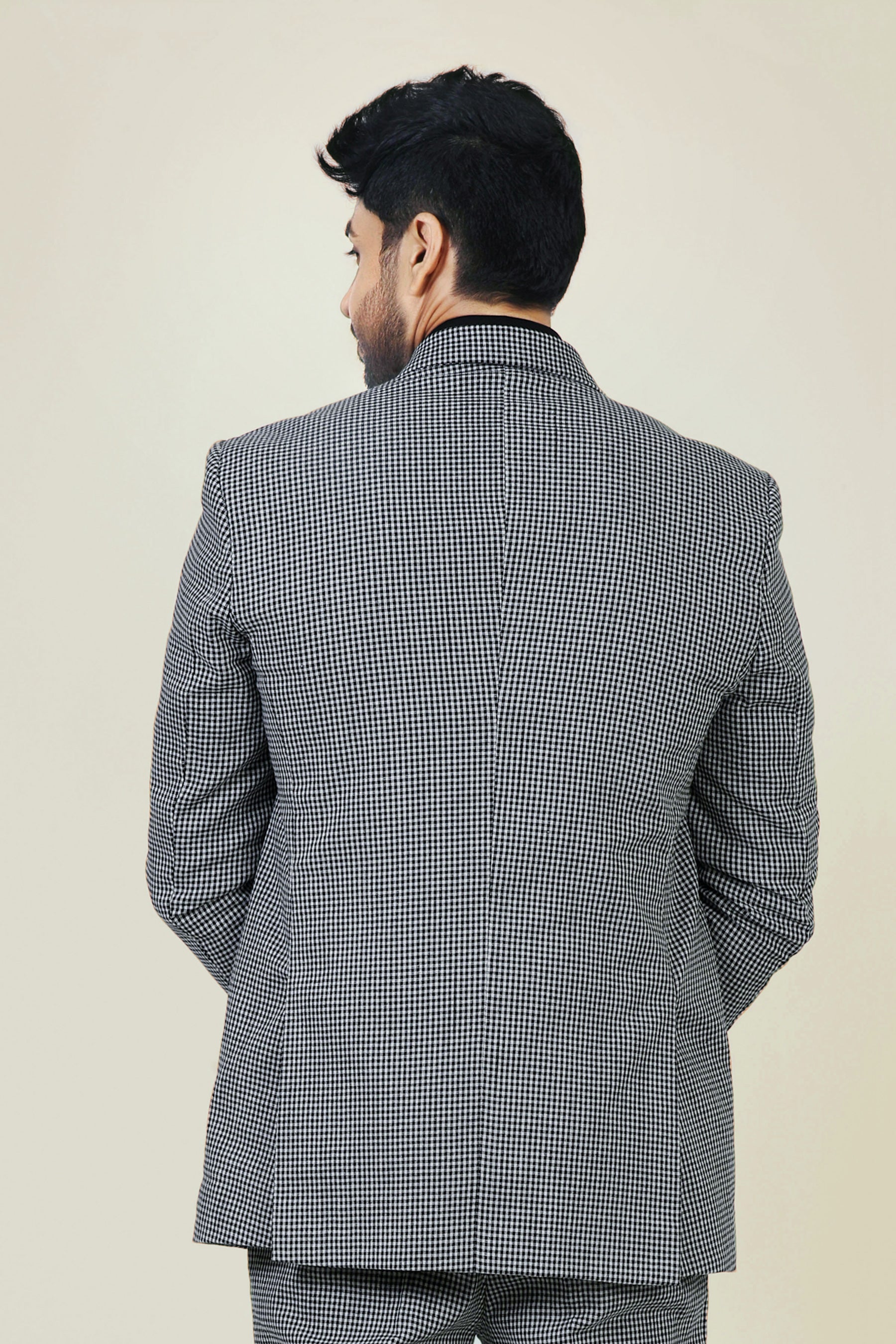 Stylish man in a gray and white checkered cotton jacket and pants, with a black shirt and white sneakers.