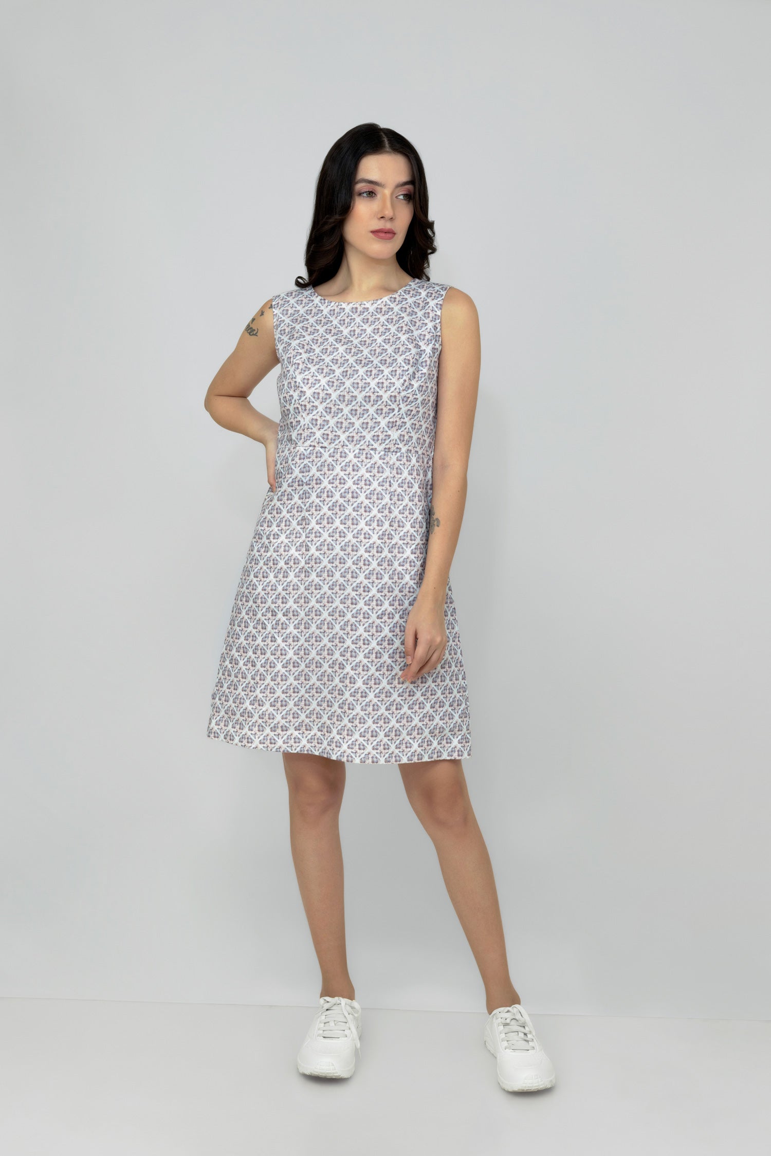 A woman models a mid-length sleeveless linen dress with a geometric pattern, featuring a boat neck and rear zip opening.
