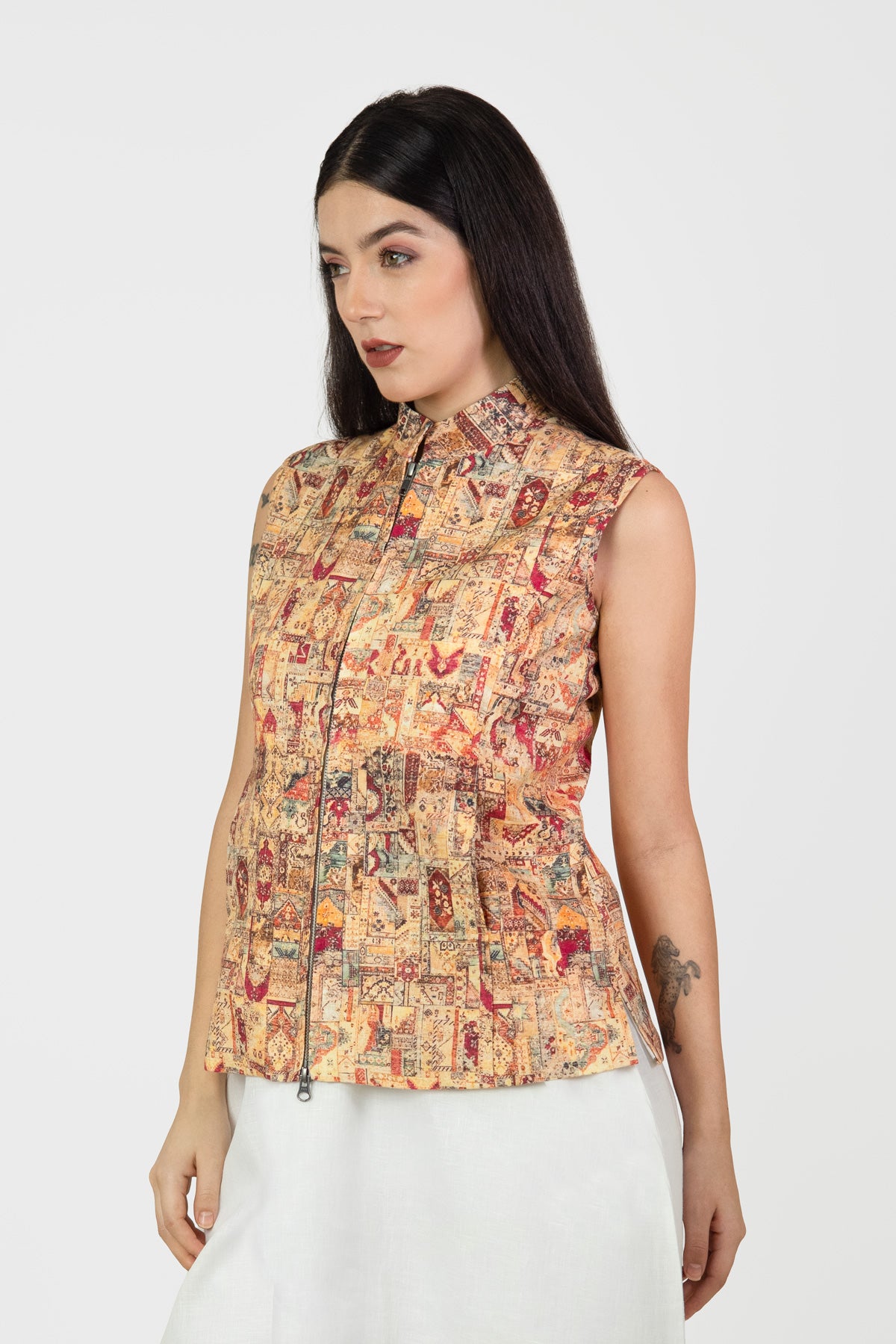 Woman wearing a sleeveless, patterned top with a plain background