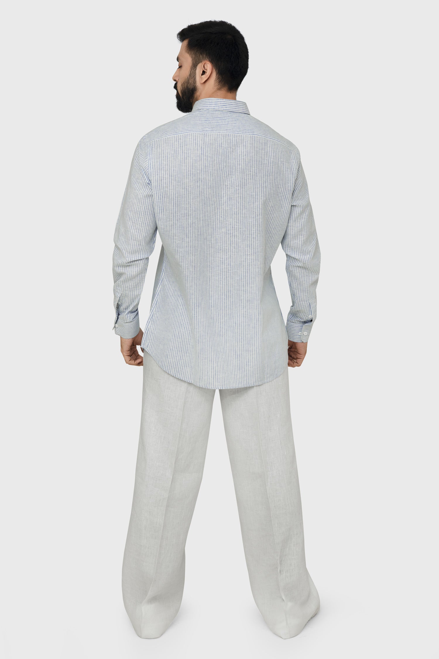 Man wearing a light gray patterned shirt and light gray pants on a white background.