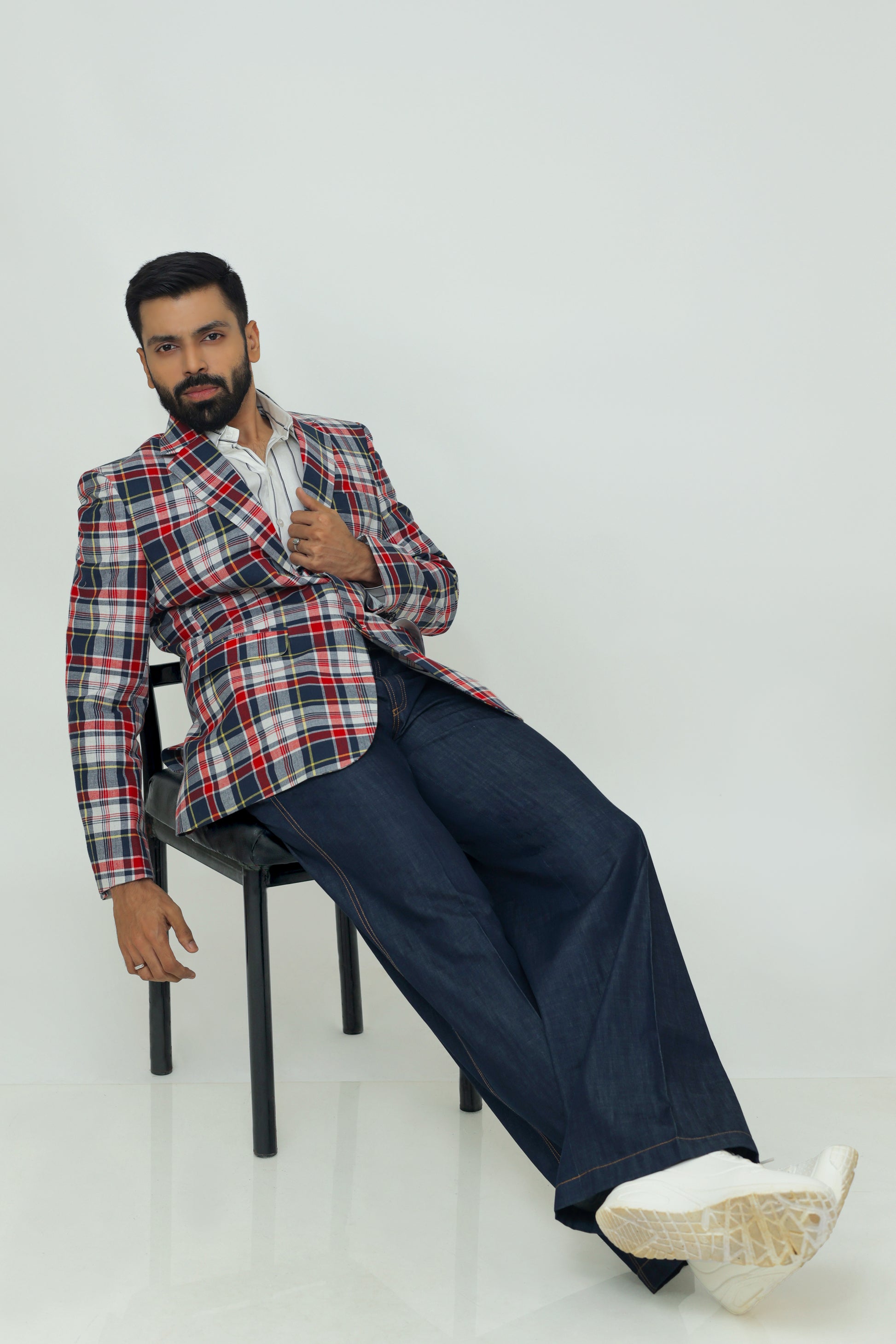 A man wearing a red, blue, and white checkered linen blazer with notch lapel, two-button front, flap pockets, and a chest pocket. He is also wearing a white shirt and dark trousers.