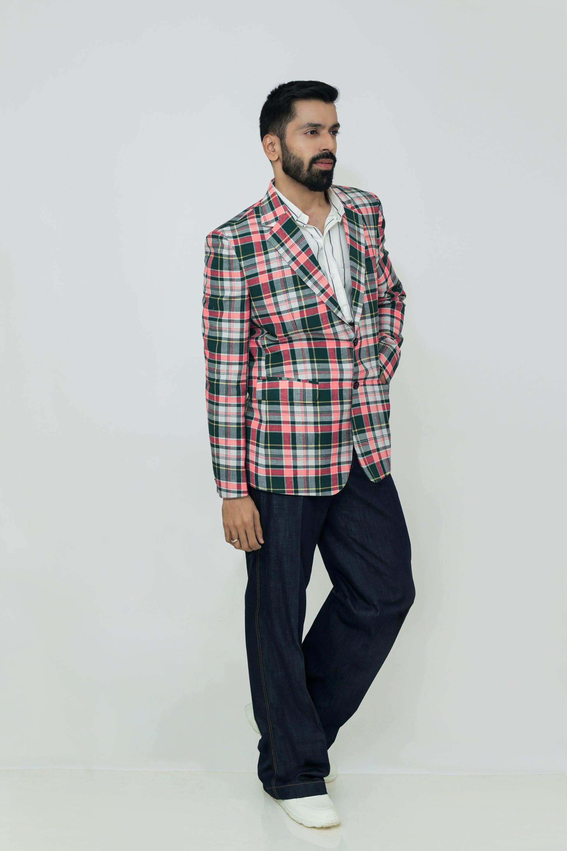 A man wearing a red, blue, and white checkered linen blazer with notch lapel, two-button front, flap pockets, and a chest pocket. He is also wearing a white shirt and dark trousers.