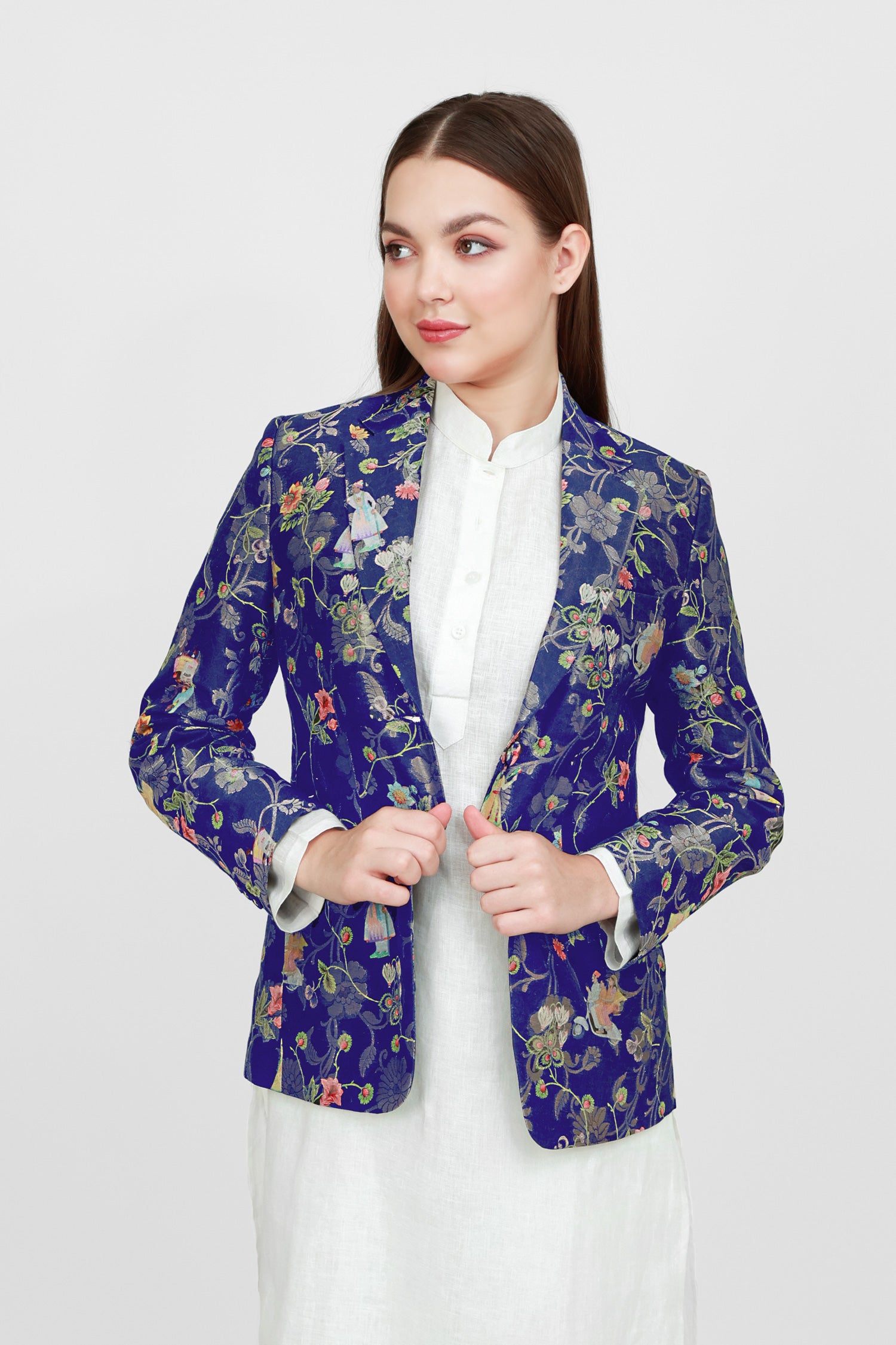 A woman modeling a silk blazer with a floral pattern, wearing a white shirt and pants.
