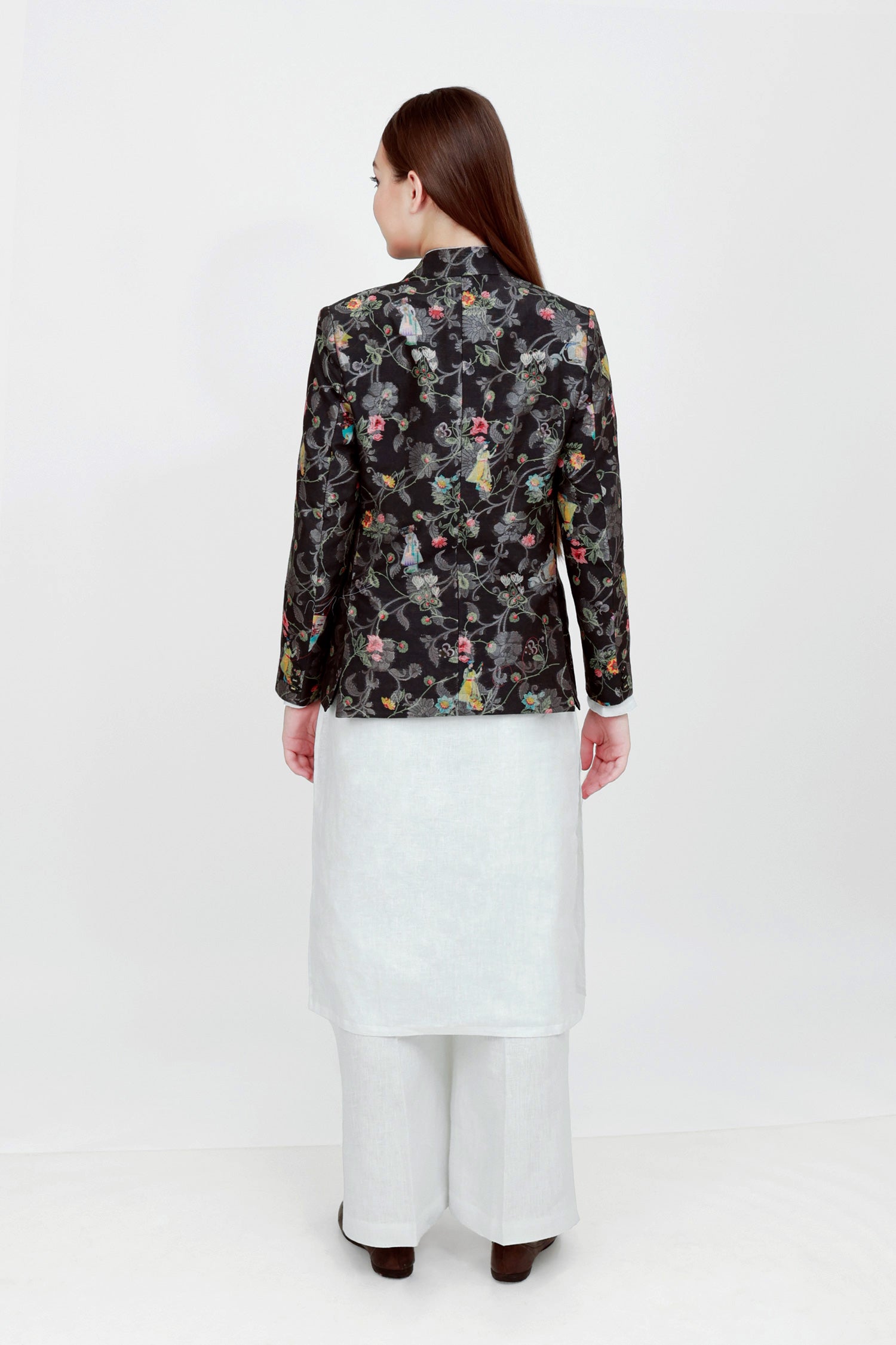 A woman modeling a silk blazer with a floral pattern, wearing a white shirt and pants.