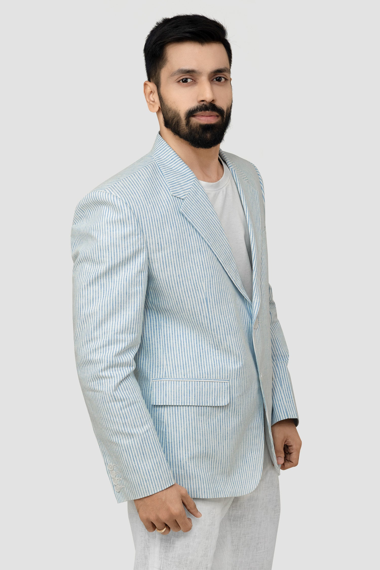 A male model wearing a light blue linen blazer with a Notch Lapel, two buttons, and two patch pockets on the front, paired with light-colored trousers.
