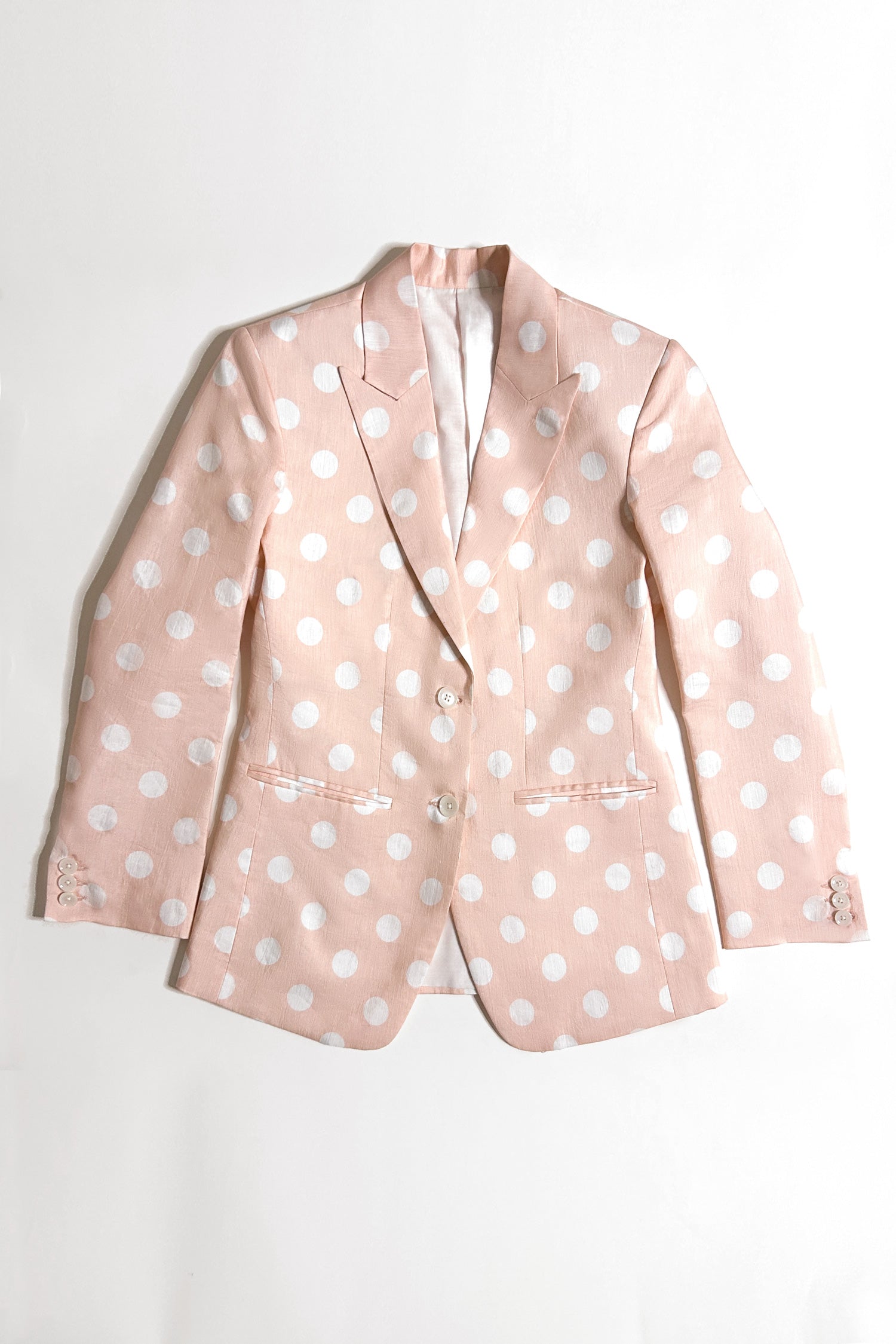 A woman peach hemp blazer with a peak lapel, two buttons, and flap pockets, paired with white trousers.