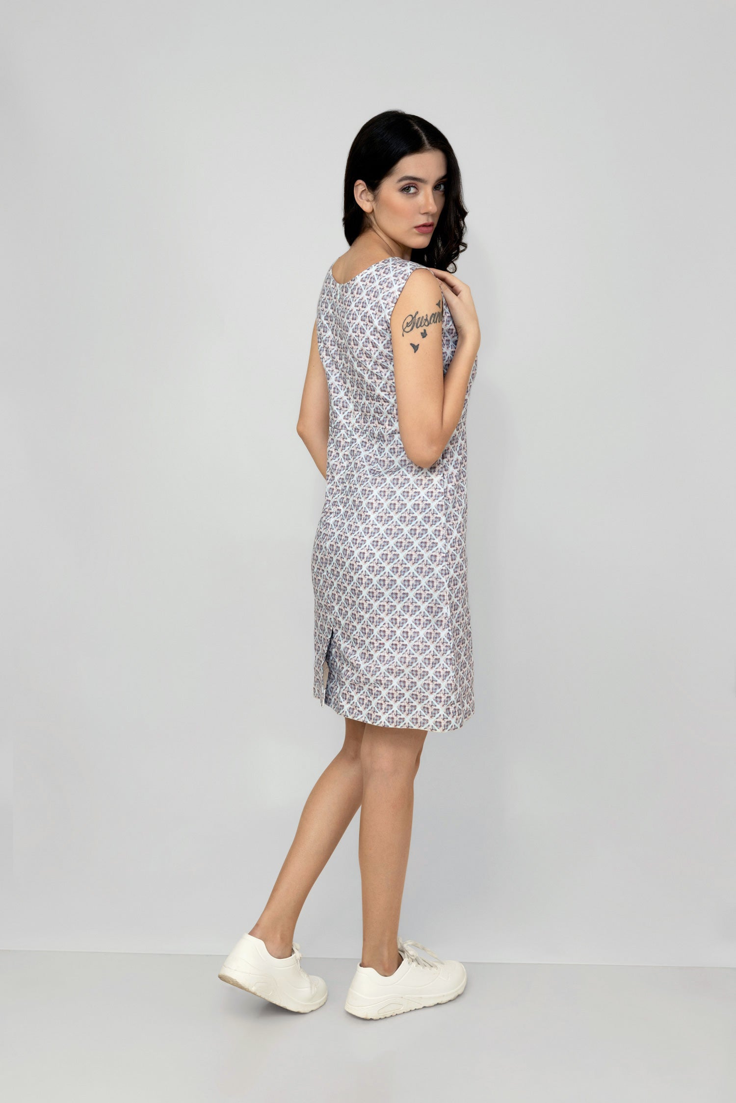 A woman models a mid-length sleeveless linen dress with a geometric pattern, featuring a boat neck and rear zip opening.
