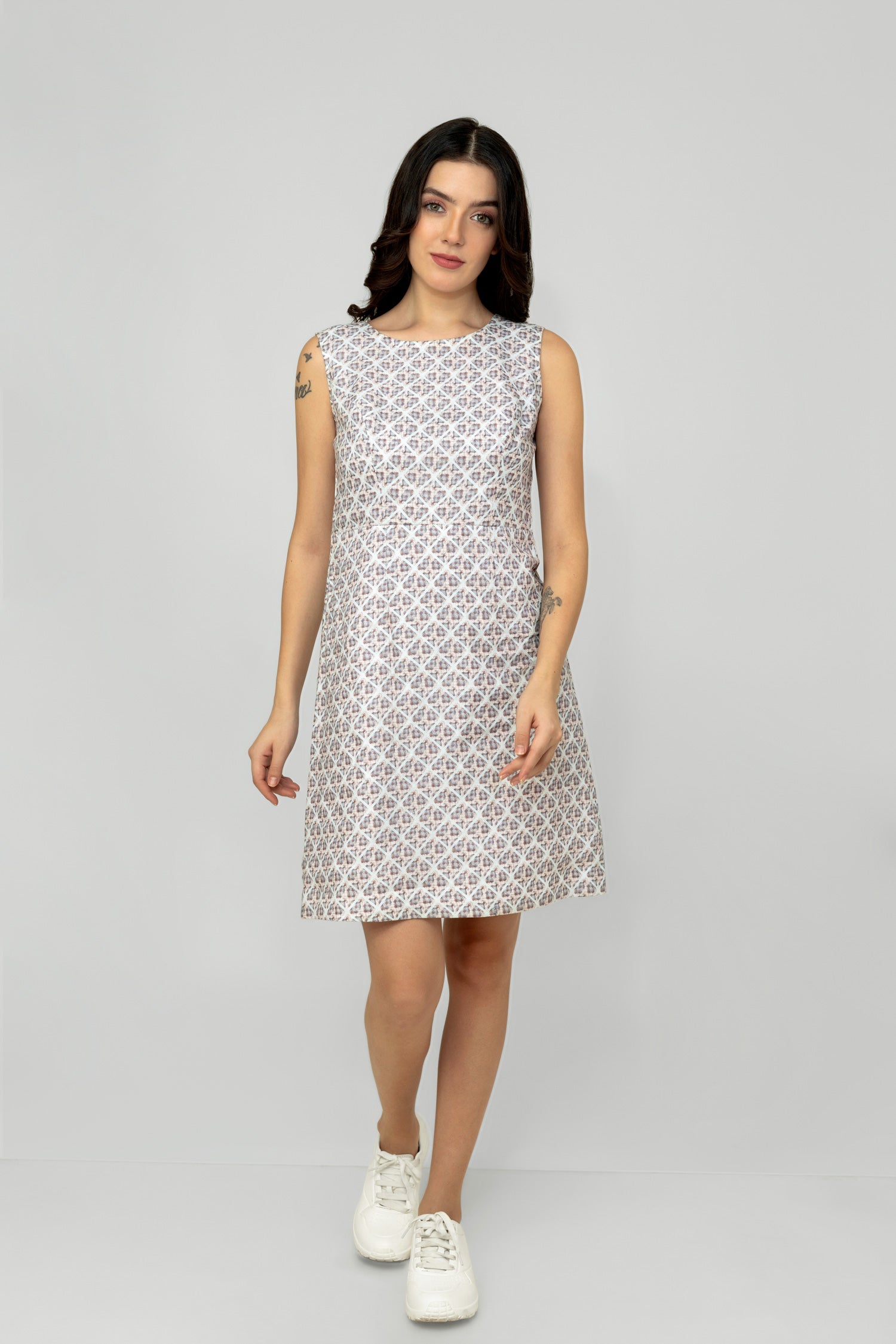 A woman models a mid-length sleeveless linen dress with a geometric pattern, featuring a boat neck and rear zip opening.
