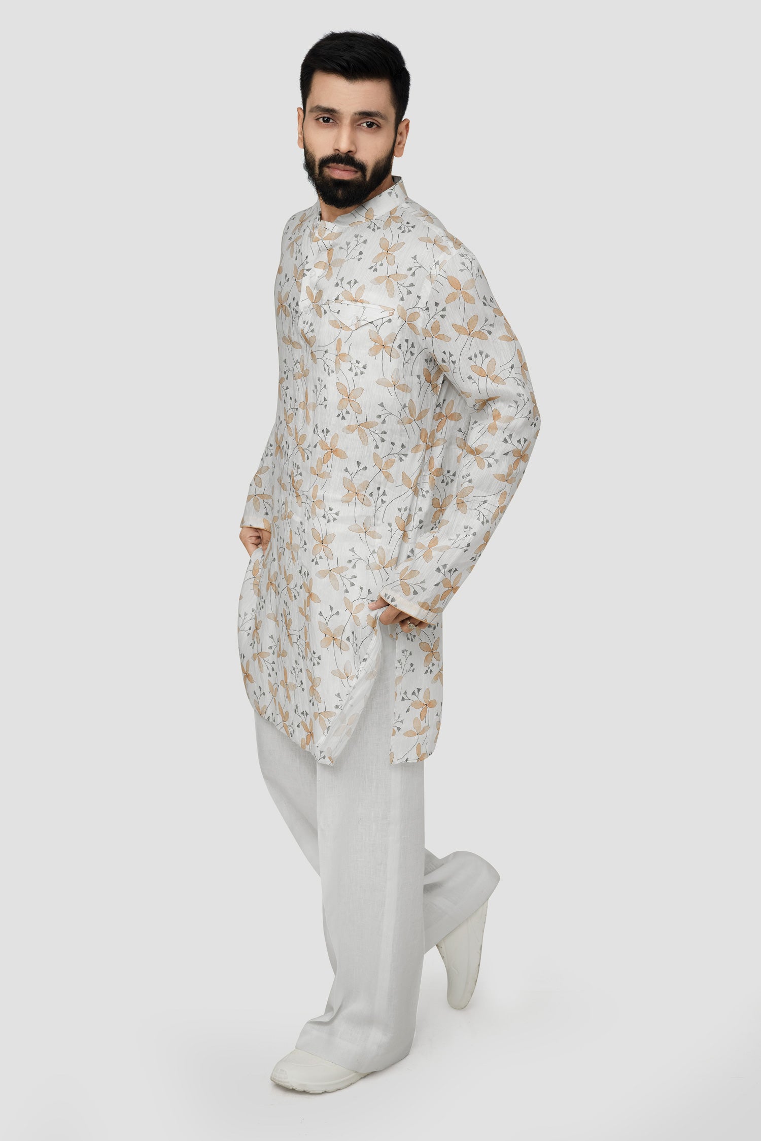 A man wearing a traditional Indian linen kurta with a mandarin collar, featuring a floral print and matching buttons, paired with light-colored trousers.