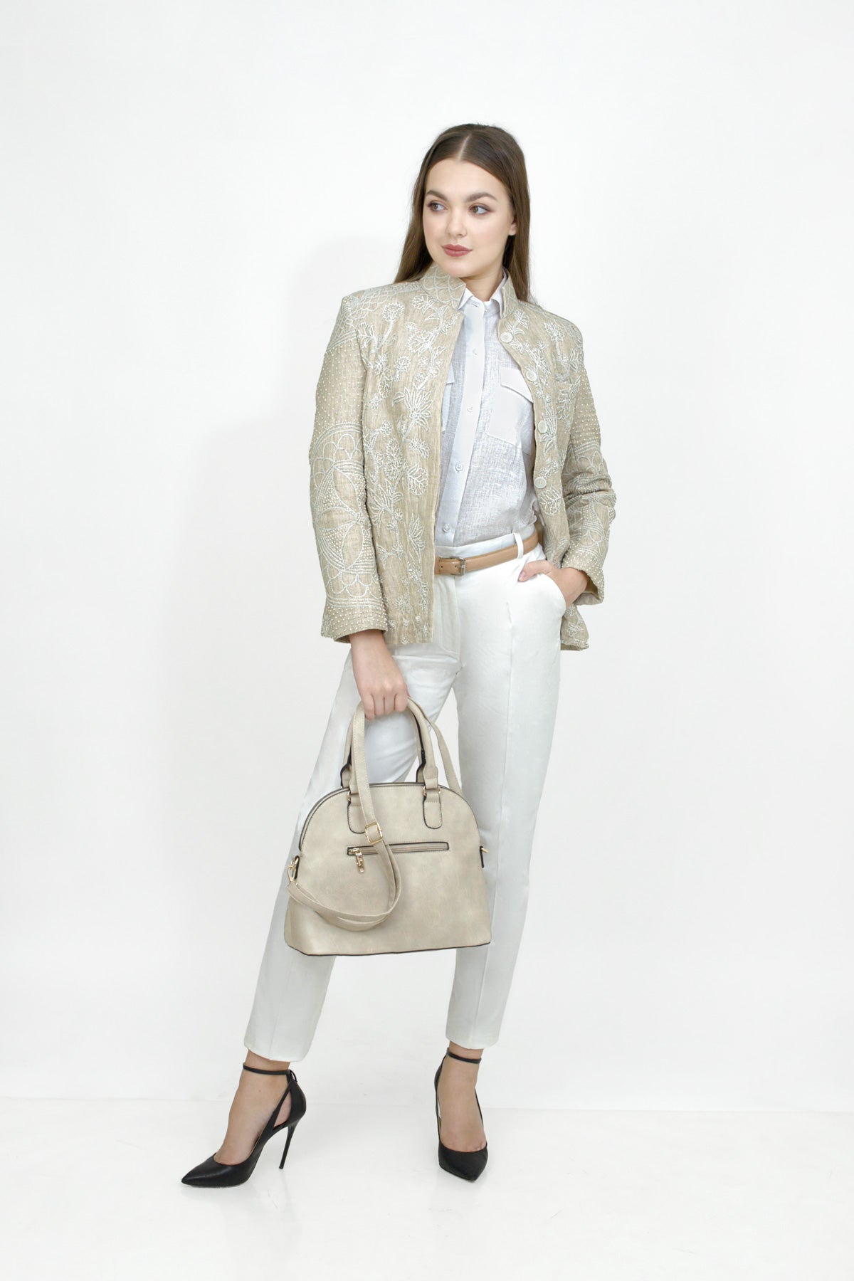 Woman in a stylish outfit with a beige blazer, white pants, and a beige handbag on a white background