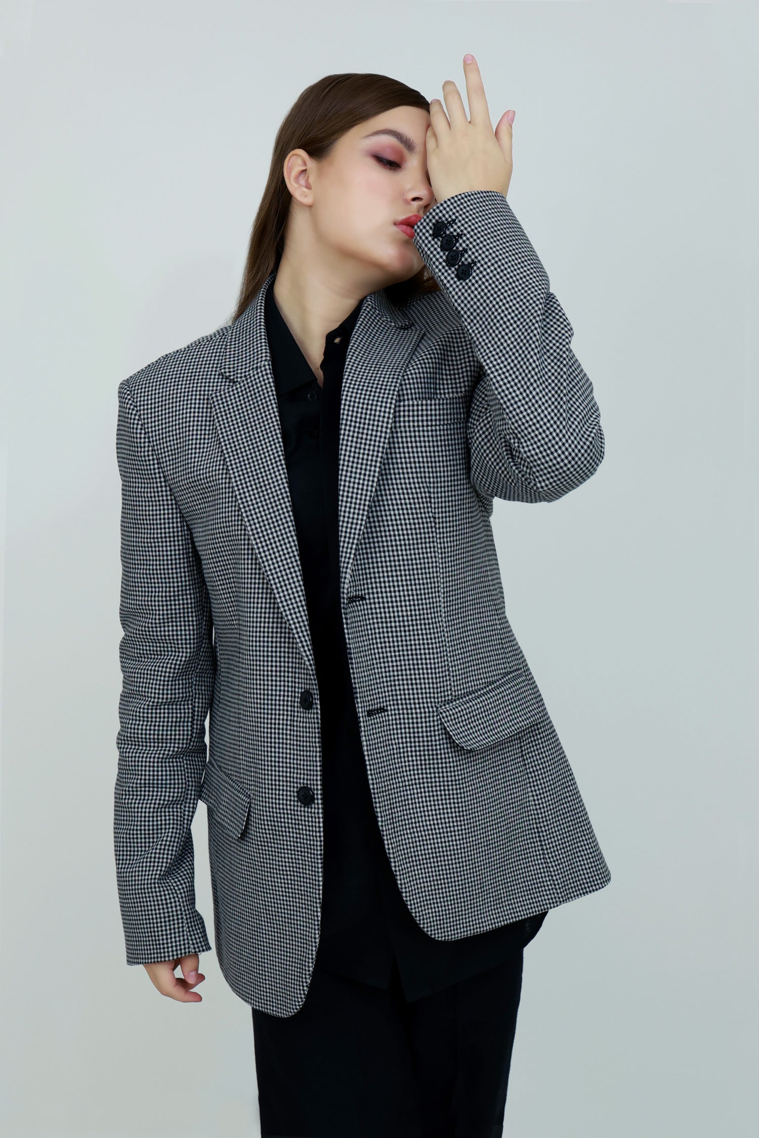 A person wearing a single-breasted, gray, checkered unisex cotton jacket with a notch lapel and functional sleeves, paired with a black outfit.