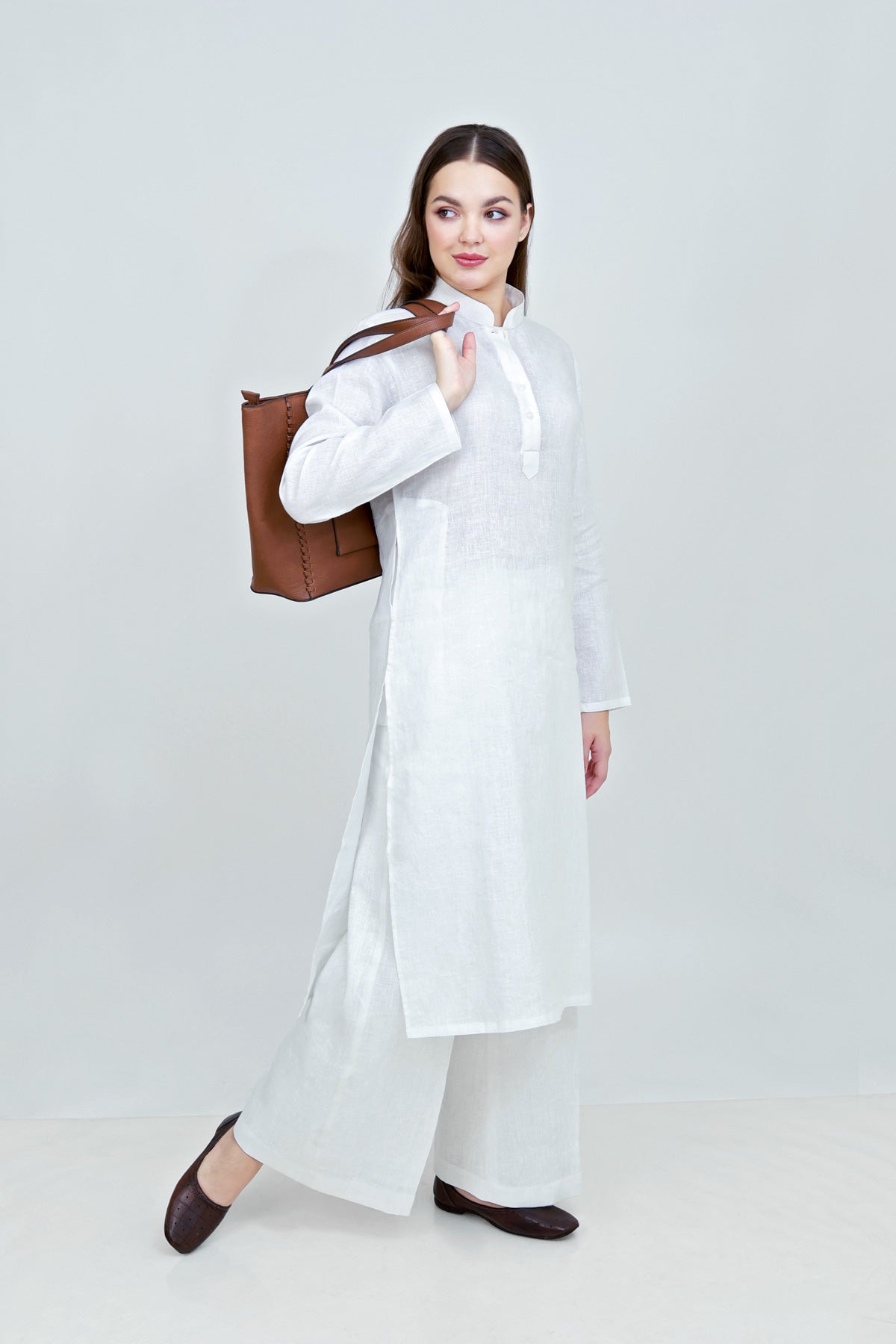 Woman in a white outfit holding a brown leather bag on a light gray background