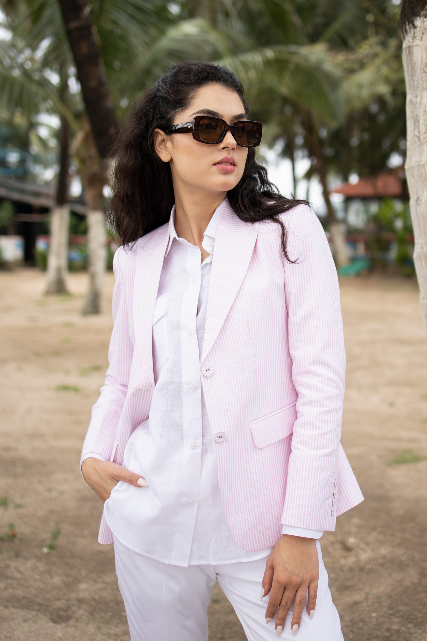 Woman in light pink blazer and white shirt outdoors with palm trees in background