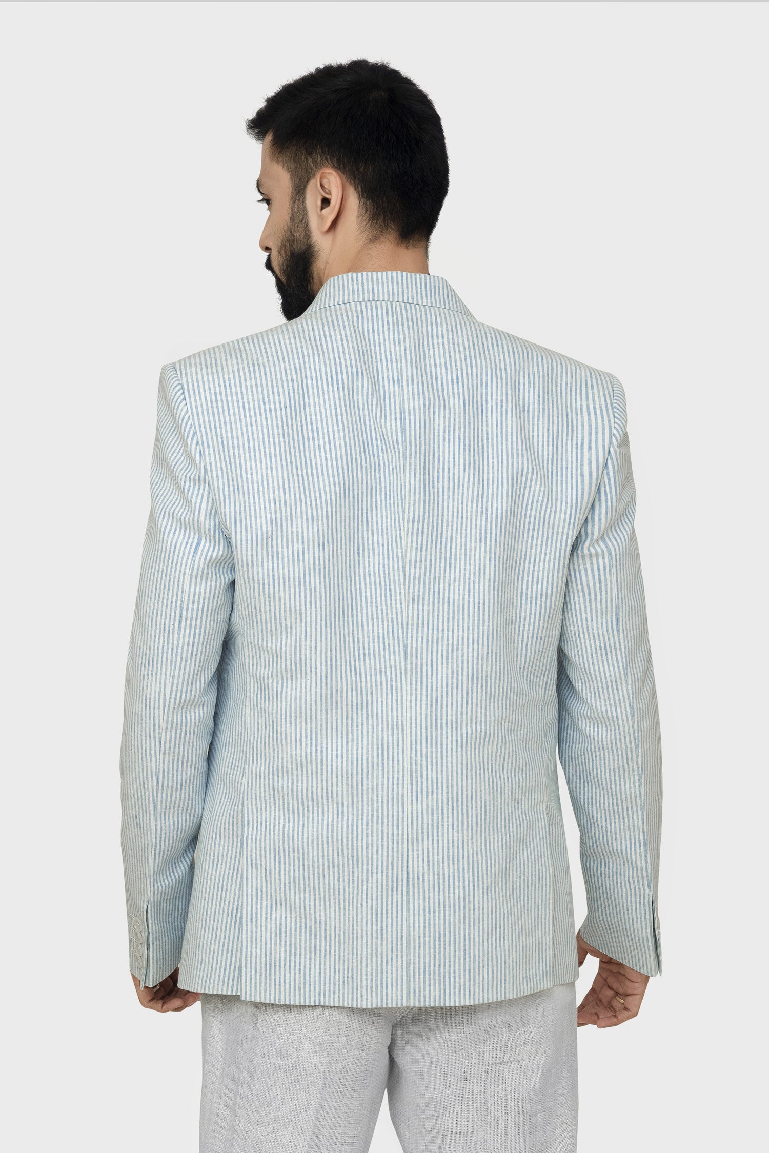 A male model wearing a light blue linen blazer with a Notch Lapel, two buttons, and two patch pockets on the front, paired with light-colored trousers.