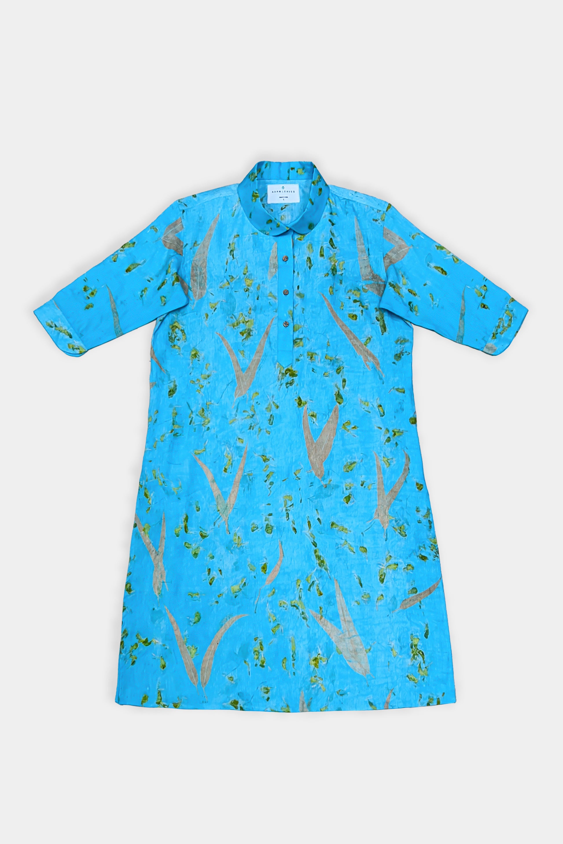 A bright blue short-sleeve shirt dress with a subtle abstract pattern of gold and green, laid flat against a light gray background.