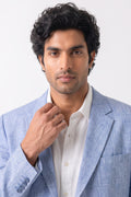 A man wearing a light blue textured blazer over a white collared shirt, posing against a clean white studio background.