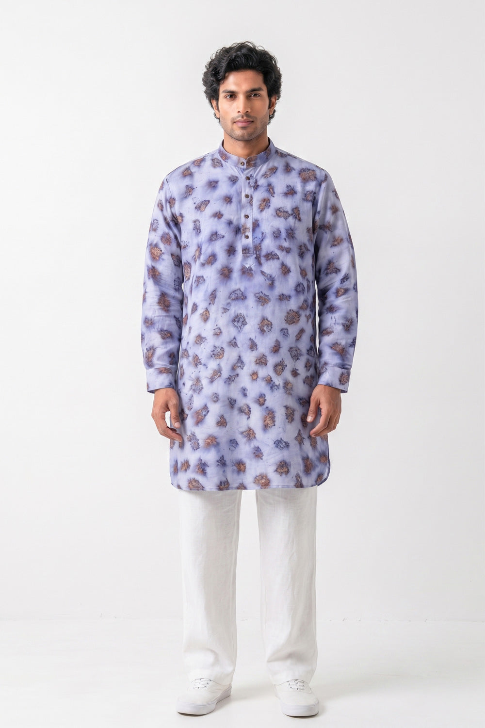 A man modeling a light purple/lavender long-sleeve kurta with a brown and purple floral pattern, paired with white trousers and white sneakers, against a plain white studio background.