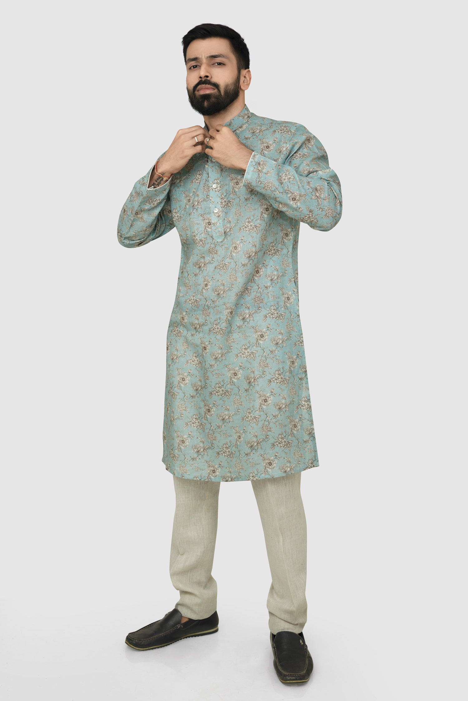 A man wearing a traditional Indian linen kurta with a mandarin collar, featuring a floral print and matching buttons, paired with light-colored trousers.