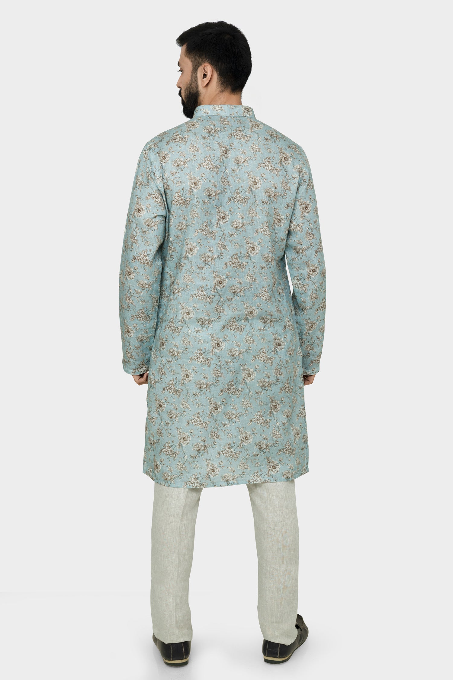 A man wearing a traditional Indian linen kurta with a mandarin collar, featuring a floral print and matching buttons, paired with light-colored trousers.