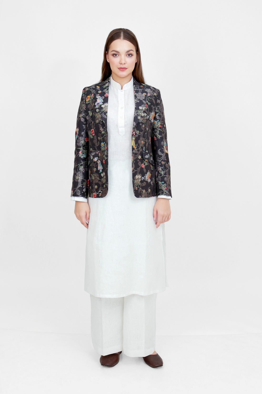 A woman modeling a silk blazer with a floral pattern, wearing a white shirt and pants.