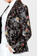 A woman modeling a silk blazer with a floral pattern, wearing a white shirt and pants.