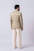 A man viewed from the back wearing a beige and white patterned hemp jacket with cream trousers, standing against a light gray studio background.