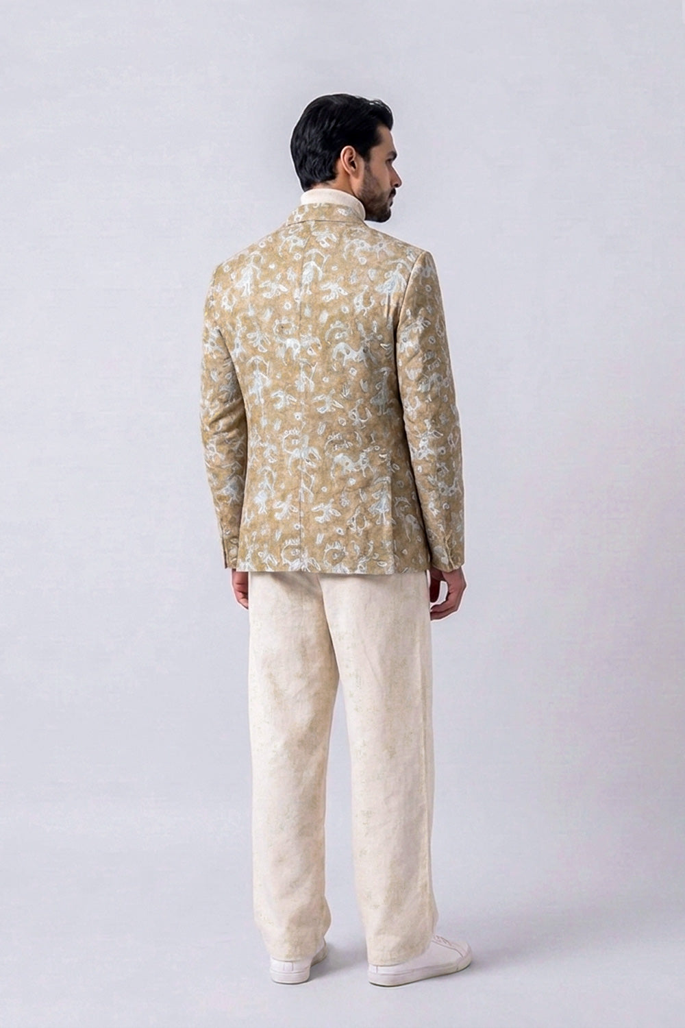 A man viewed from the back wearing a beige and white patterned hemp jacket with cream trousers, standing against a light gray studio background.