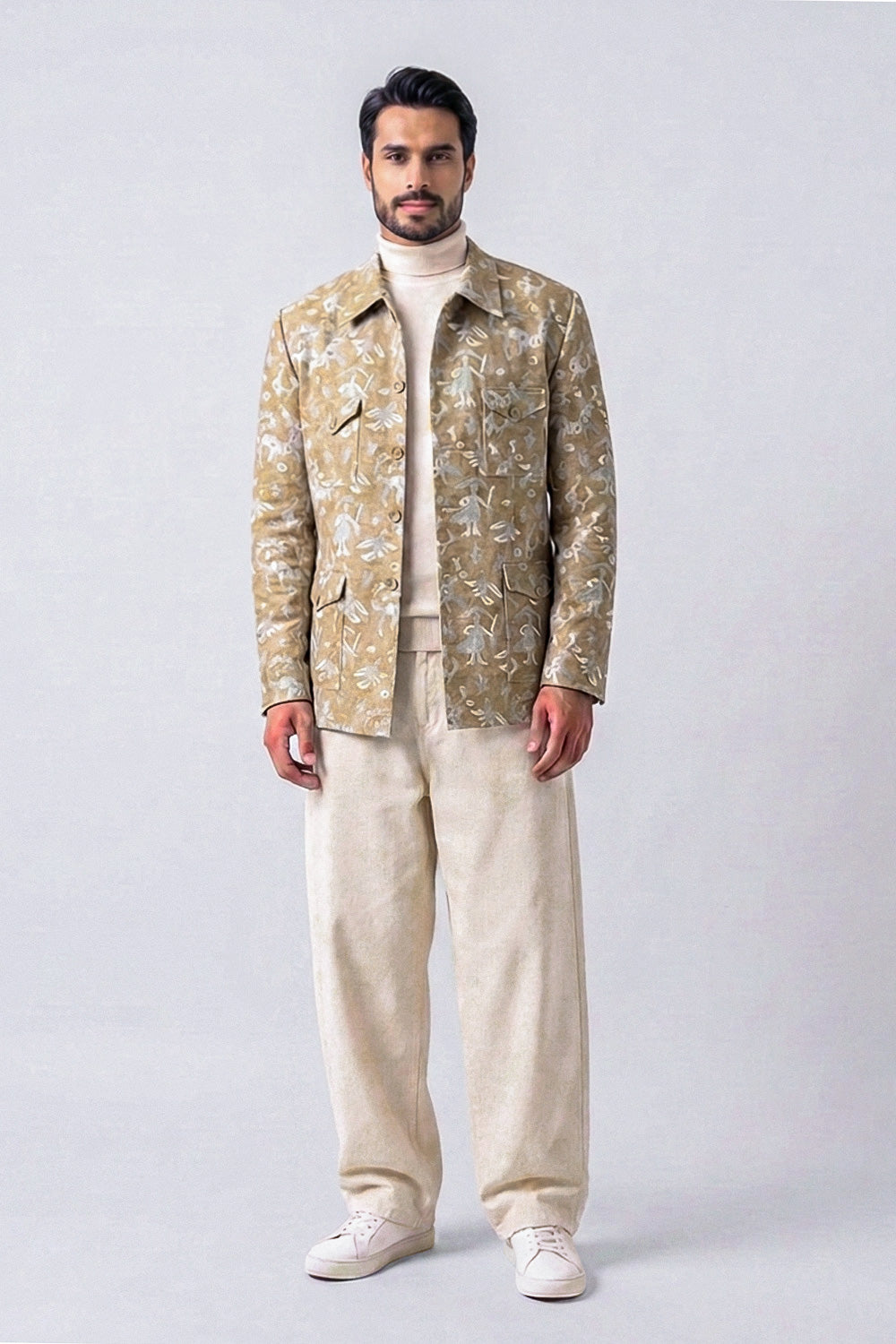 A man shown in front profile wearing a beige and white patterned hemp jacket, cream trousers, and white sneakers, standing against a light gray studio background.