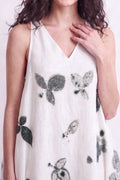 A woman wearing a sleeveless white V-neck dress with a black and gray botanical leaf print, shown from the shoulders to the hips against a plain light background.
