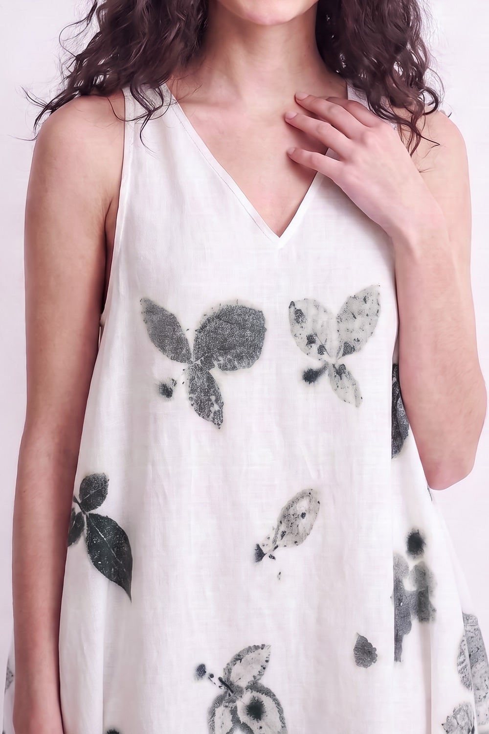 A woman wearing a sleeveless white V-neck dress with a black and gray botanical leaf print, shown from the shoulders to the hips against a plain light background.