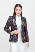A woman modeling a silk blazer with a floral pattern, wearing a white shirt and pants.