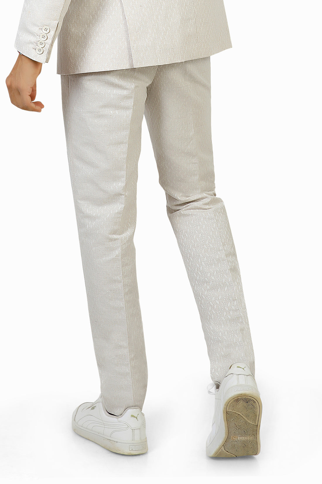 A man wearing white linen trousers with a white jacket and a multicolored shirt, standing against a white background.