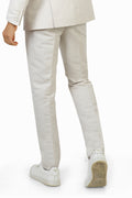 A man wearing white linen trousers with a white jacket and a multicolored shirt, standing against a white background.